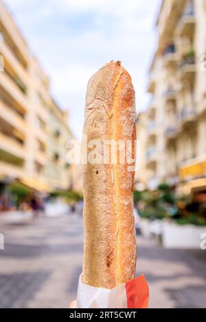 Woman s hand holding a freshly baked rustic French baguette bread from an artisanal bakery, a background of blurred buildings in Old Town Nice, France Stock Photo