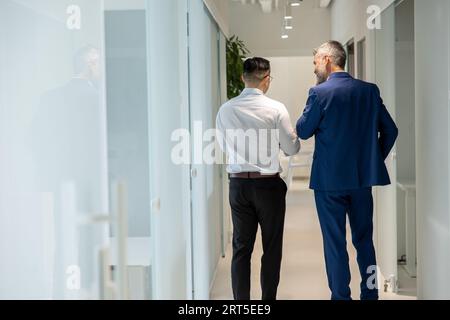 Men walking along corridor in office and talking about their work. Stock Photo