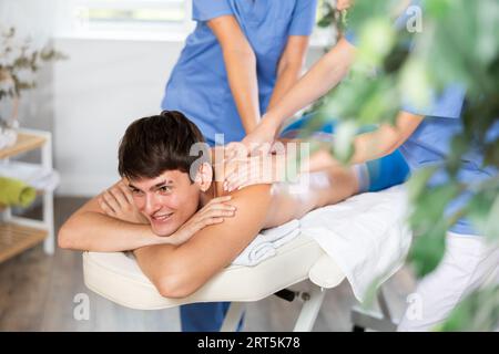Two unrecognizable female masseuses perform stroking and rubbing of muscles of back to guy client Stock Photo