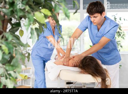 Two unrecognizable female and male masseuses perform stroking and rubbing of muscle of back to girl Stock Photo