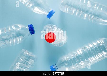 Crushed plastic water bottles with blue caps standing around crushed plastic water bottle with red cap on blue background Stock Photo