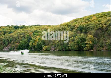 Two people riding water scooter on river with beautiful green trees background. Speed, sport, vacation, extreme Stock Photo