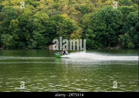 Two people riding jet ski watercraft on river with beautiful green trees background. Speed, sport, vacation, extreme Stock Photo