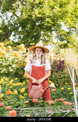 A woman in a sunhat and red romper watering her cut flower garde Stock Photo
