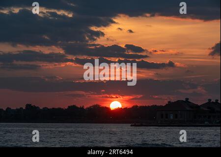 The setting sun behind the silhouetted trees and water creates a dramatic cloudscape. Stock Photo