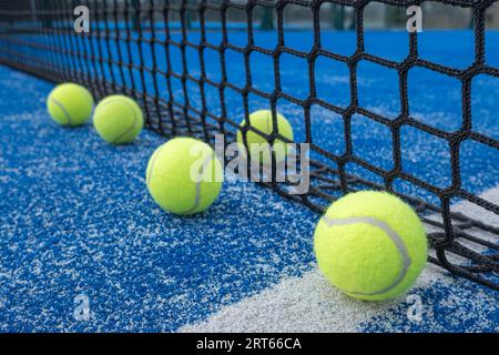 Four yellow balls on floor in front and one behind of paddle net in blue court outdoors. Padel tennis court Stock Photo