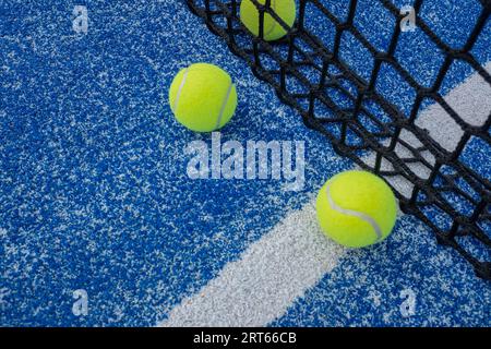 Three yellow balls on floor in front and behind of paddle net in blue court outdoors. Padel tennis Stock Photo