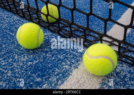 Three yellow balls on floor in front and behind of paddle net in blue court outdoors. Padel tennis court Stock Photo