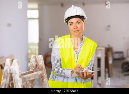 Female architect with papers taking notes in building under renovation Stock Photo