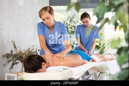 Two professional masseuses performing back massage for male patient Stock Photo