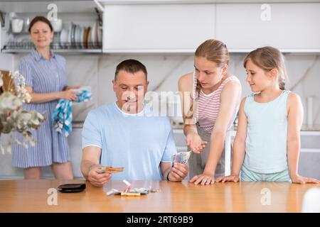 Father gives pocket money to children and wife in kitchen Stock Photo