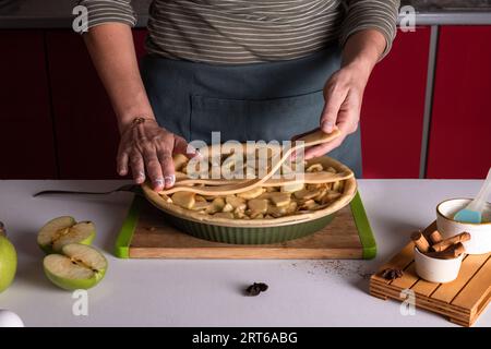 Woman placing pie dough on top of the apple pie in the bakery dish, ready to be put in the oven, preparing apple pie. Thanksgiving tart preparation, a Stock Photo