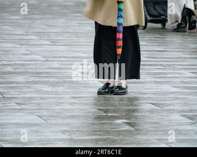 Against a soft bokeh backdrop, an anonymous woman stands front-facing, elegantly garbed in a trench coat while holding an umbrella Stock Photo