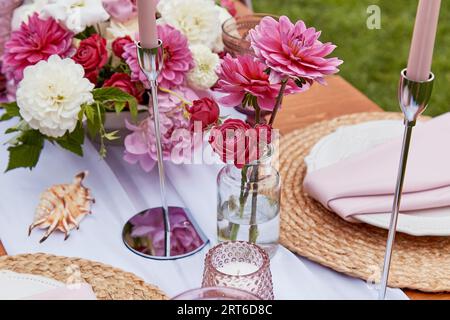 Picnic aesthetics table setting, flowers arrangement, shells. Cozy setup with flowers and candles. Stock Photo