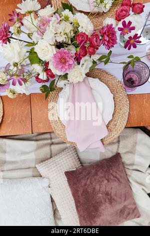 Aesthetics pink cozy picnic, served table with flowers bouquets, dishes, pillows top view. Stock Photo