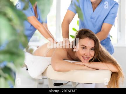 Two unrecognizable female and male masseuses perform stroking and rubbing of muscle of back to girl Stock Photo