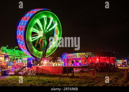 An outdoor ferris wheel illuminated against a backdrop of a vibrant, green landscape Stock Photo