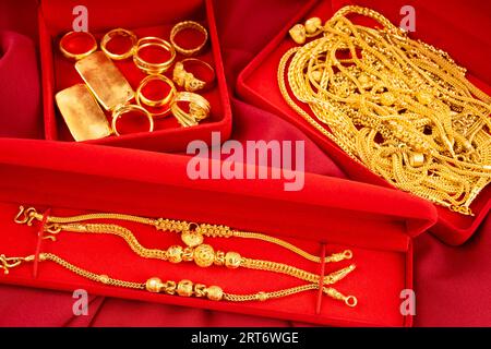 Many gold necklaces and gold bars in red box on red velvet cloth background. Stock Photo