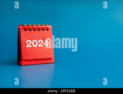Happy new year 2024 banner background. 2024 white numbers year on red small desk calendar cover standing on blue background with copy space. Business Stock Photo