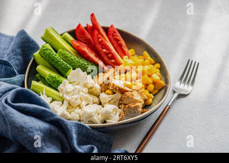 High angle of five ingredients bowl with raw organic vegetables cauliflower, tomato, cucumber, boiled sweet corn and barbeque chicken meat placed on g Stock Photo