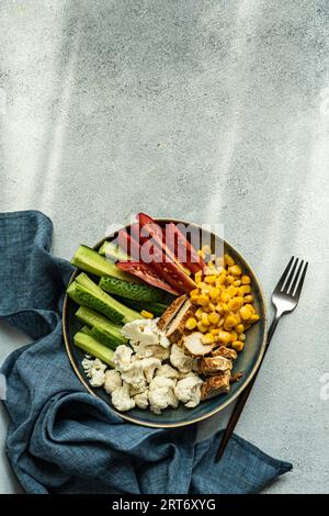 Top view of five ingredients bowl with raw organic vegetables cauliflower, tomato, cucumber, boiled sweet corn and barbeque chicken meat placed on gra Stock Photo