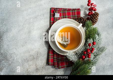 Top view of Christmas cup of tea placed on red napkin near holly and pine cones on gray table Stock Photo