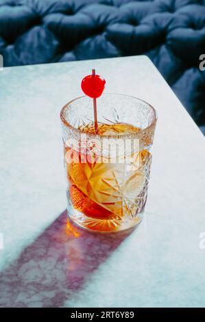 High angle of glass filled with alcoholic old fashioned whiskey and ice cubes garnished with cherries placed on table Stock Photo