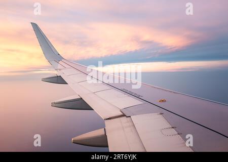 Breathtaking view of white wing of aircraft flying in blue sky over colorful fluffy cumulus clouds in sunset Stock Photo