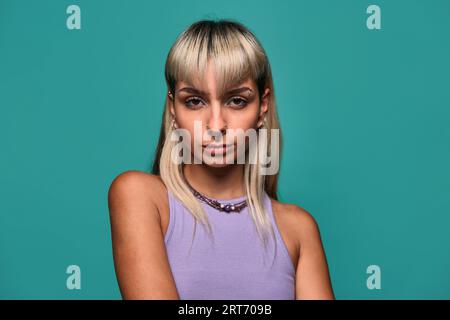 Young female with blond hair and piercing standing against turquoise background Stock Photo