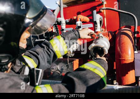 Crop anonymous firefighter in professional uniform and protective helmet working and checking fire fighting equipment under sunlight Stock Photo