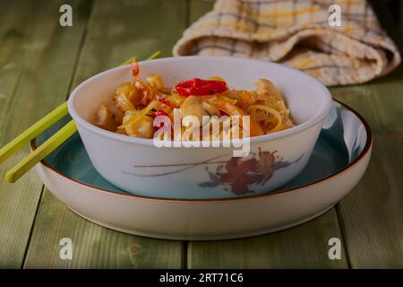 Chicken noodle stir fry in a bowl with chopsticks at the side on a wooden table. Stock Photo