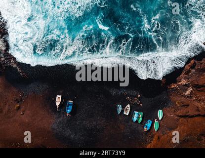 Horizontal aerial photo of black sand volcanic beach with boats on the shore and big and strong waves in ocean -  Lanzarote, Canary Islands. Waves in Stock Photo