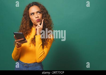 Serious young woman taps chin while thinking, contemplating, green studio Stock Photo