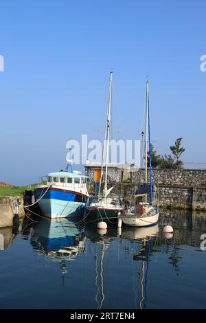 Carnlough, County Antrim, N. Ireland: Boats moored in still reflective waters of harbour against backdrop of blue skies Stock Photo