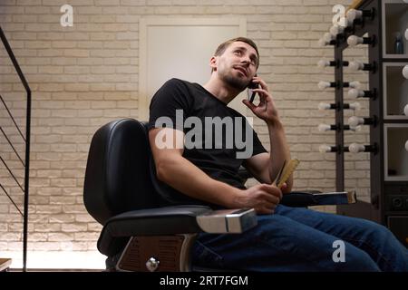 The guy is talking on phone, sitting in hairdresser's chair Stock Photo