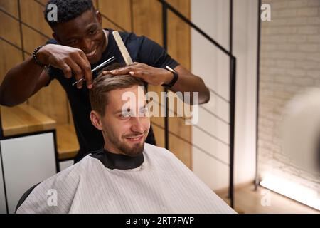 Young African American hairdresser cuts a clients scissors Stock Photo