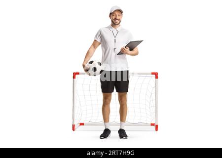 Full length portrait of a football coach holding a ball and a clipboard in front of a mini goal isolated on white background Stock Photo