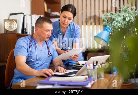 Two focused physicians working with case histories on laptop Stock Photo