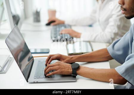 Hands of software developer with smartwatch working on laptop in office Stock Photo