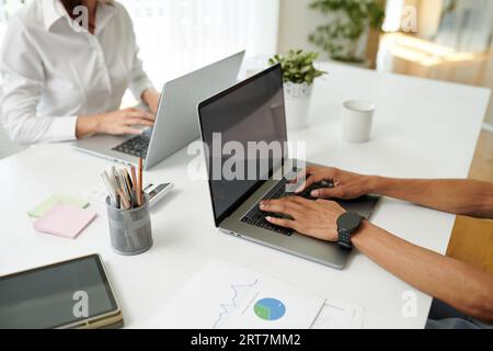 Hands of businessman working on laptop in office when sitting against coworker Stock Photo