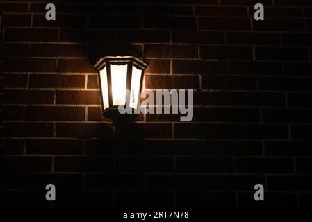 Retro-style lamp hangs on a red brick wall at night, copy space. Stock Photo