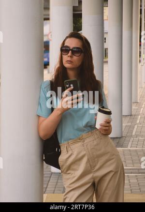 girl on the street holding a phone and a paper cup of coffee Stock Photo