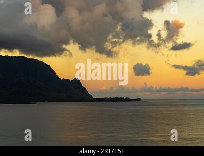 Rising sun illuminates rain clouds over the mountain peaks of Na Pali coast across Hanalei Bay on Kauai Stock Photo