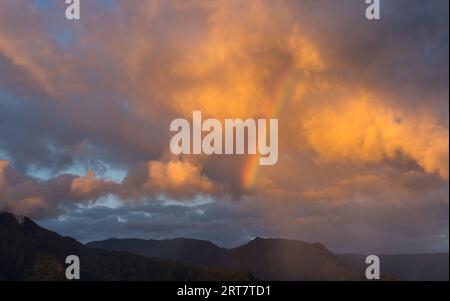 Sunrise illuminates storm clouds and rainbow over Hanalei mountains from Princeville overlook of bay Stock Photo