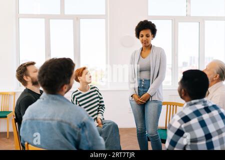 Portrait of African black female patient having breakthrough in group therapy session, standing by diverse and different ages sitting in circle. Stock Photo