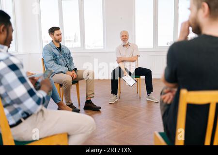 Portrait of friendly mature male mentor corporate leader communicating with multiracial business professional team, teaching interns staff group Stock Photo