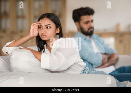 Unhappy indian couple having quarrel, depressed man and woman sitting on couch, experiencing difficulties in marriage Stock Photo