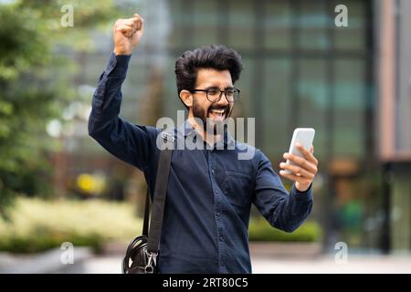 Excited eastern businessman looking at phone screen, gesturing Stock Photo