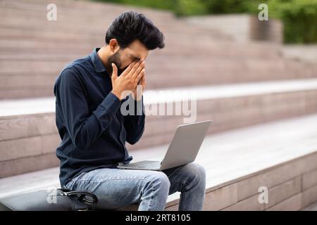 Tired young indian guy working on laptop at park Stock Photo