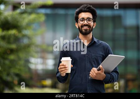 Portrait of cheerful indian guy with laptop and takeaway coffee Stock Photo
